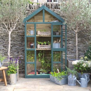 small greenhouse painted with wooden frame positioned in front of a slate wall