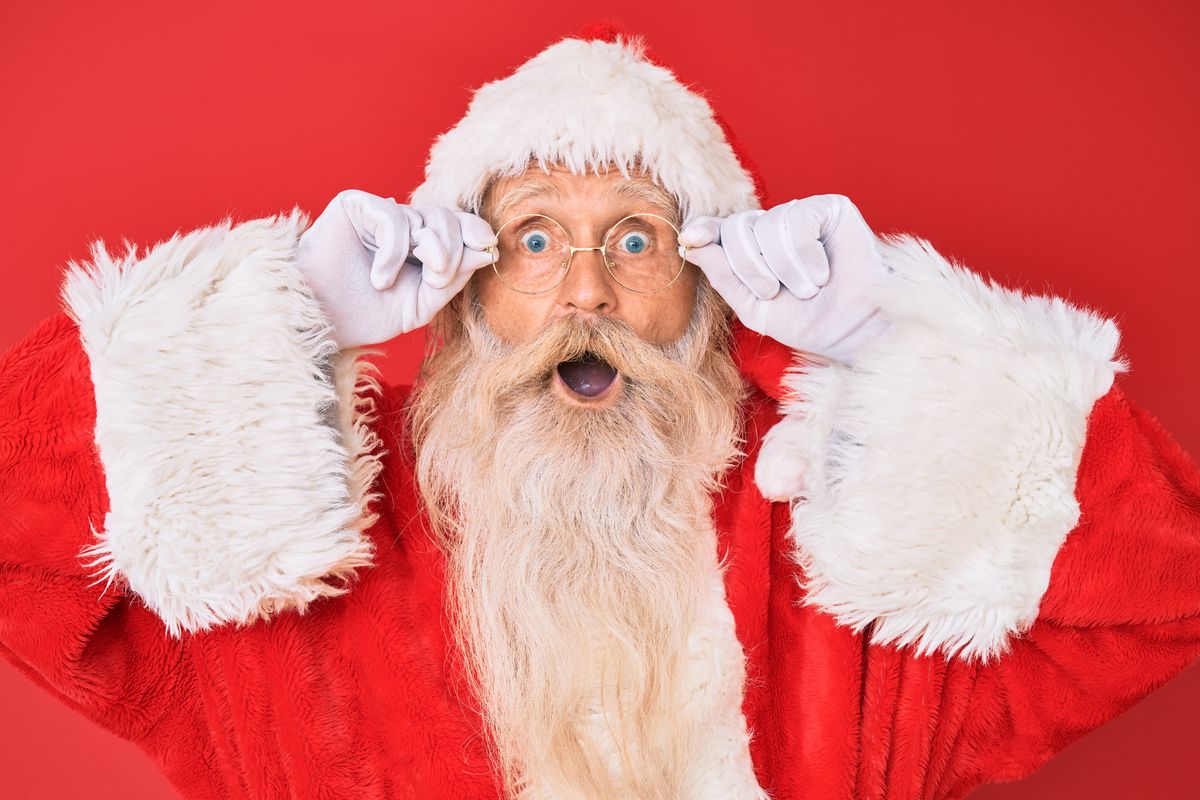 Father Christmas - an old man with white hair and a long white beard wearing a red fur-trimmed hat and coat and circular glasses - holds his glasses and opens his mouth in a shocked expression