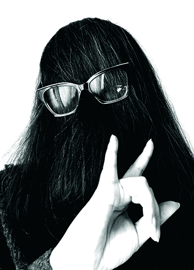 Noiry headshot; a woman with her hair covering her face wearing glasses over the hair