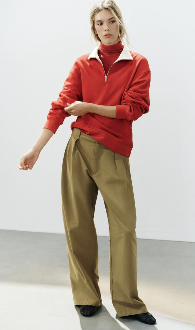 Zara early autumn colour trends 2026. The model wears olive trousers with a red jumper and black mesh ballet flats.