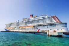 Carnival cruise ship docked in turquoise water Caribbean sea under clear blue sky with lifeboats along white hull near pier.