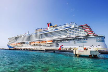 Carnival cruise ship docked in turquoise water Caribbean sea under clear blue sky with lifeboats along white hull near pier. 