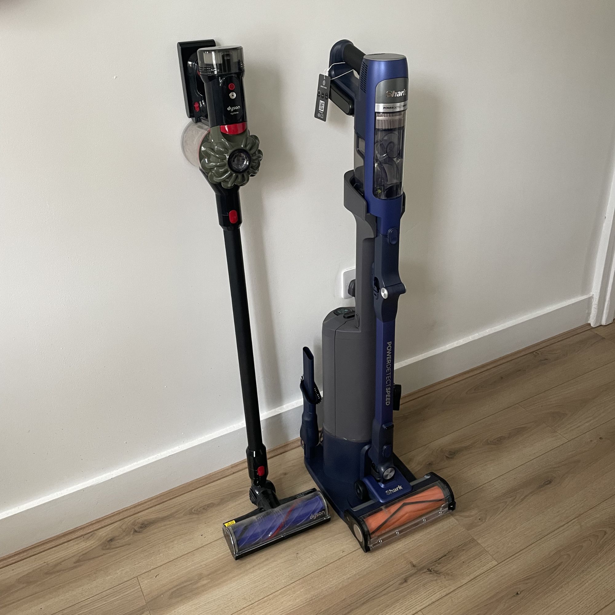 Shark PowerDetect Speed Clean and the auto-dock leaning up against a white wall next to the Dyson V8 Cyclone