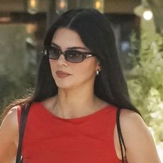 Kendall Jenner wearing a red high neck dress, black sunglasses, and a striped tote bag