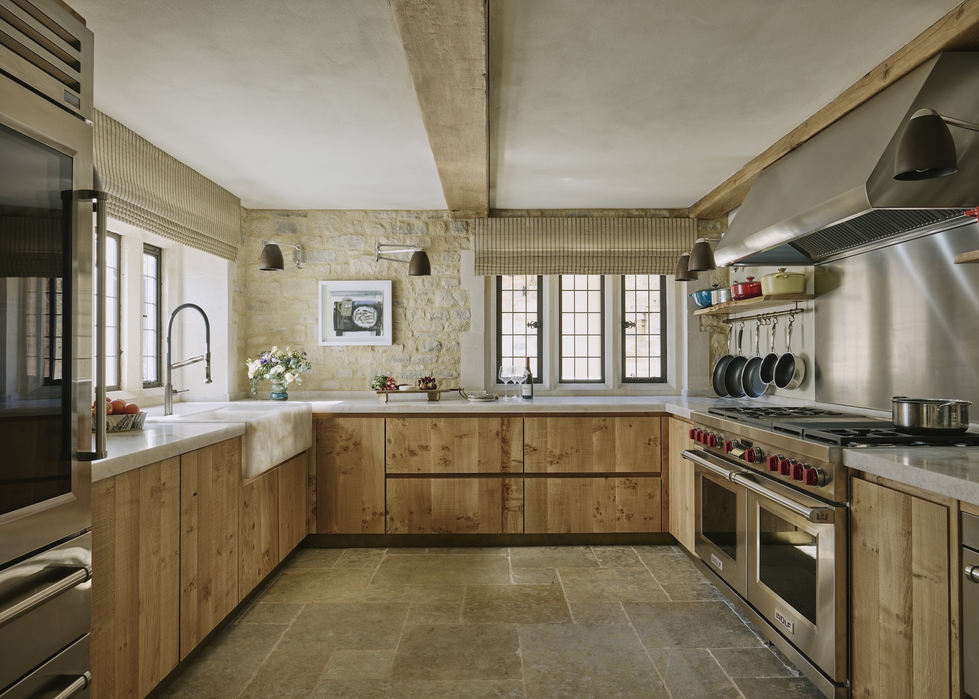 A large oak kitchen with a large gas oven and stove as well as a range hood, a kitchen sink and cabinets all around the lower part of the kitchen.