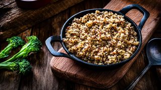 Black cast iron bowl full of quinoa, resting on wooden chopping board