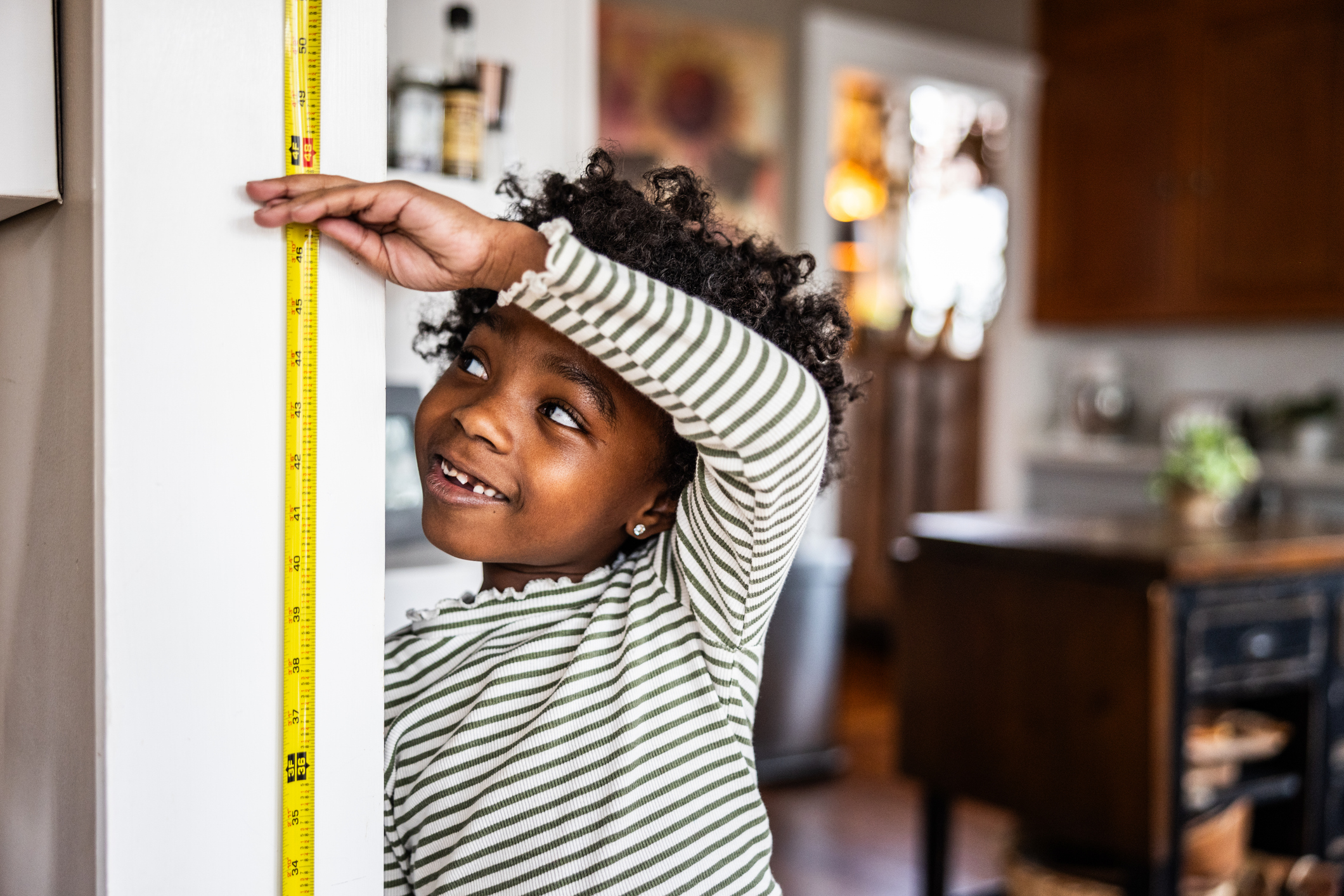 Young girl checking her height on the wall, demonstrating her growth in height over time.