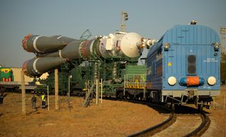 A blue train carries a white-tipped green/grey Soyuz rocket along train tracks. MS-24, Sept. 12, 2023.