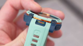 Close up of Garmin Instinct 3 GPS smartwatch in Neotropic/Twilight with a grey and orange case and sea foam green strap