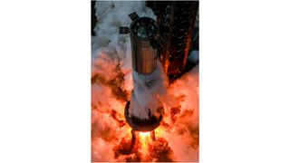 aerial view of a large silver rocket firing its engines on a launch mount