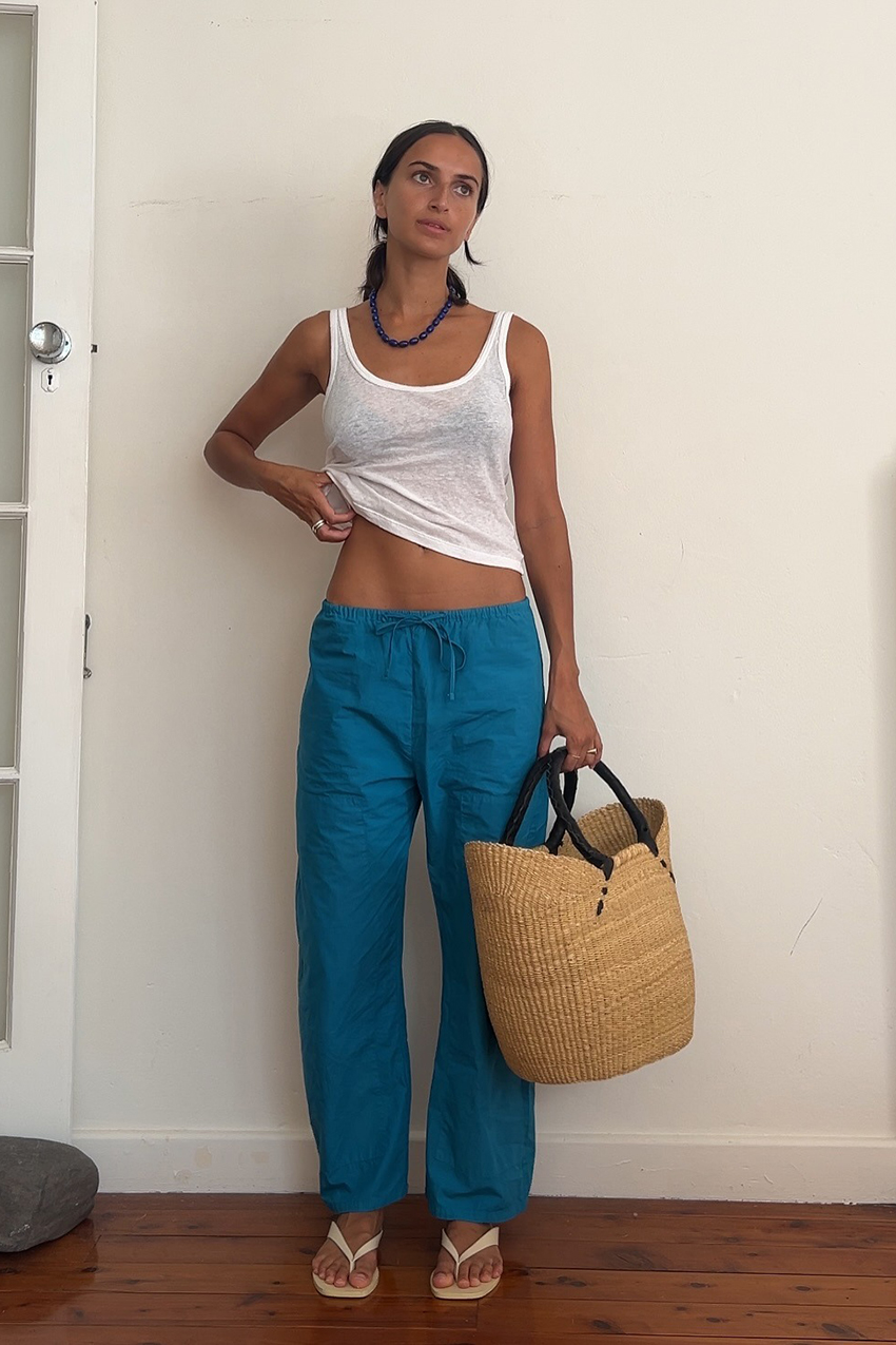 a woman wearing a white tank top, blue pants, and white sandals