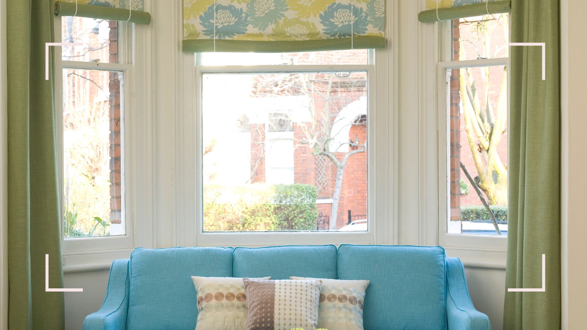 Living room bay window dressed with blue and green patterned roller blinds and green curtains