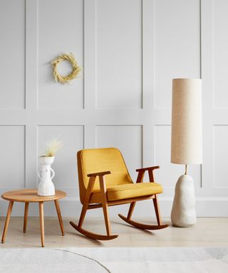 Light grey wall paneling with walnut and mustard rocking chair and sculptural floor lamp.