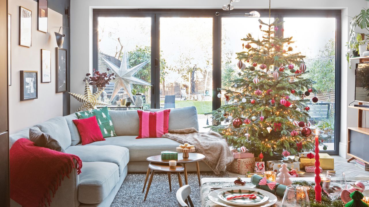 Open plan living dining room with grey corner sofa by sliding doors and a brightly decorated Christmas tree