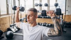 Man lifting dumbbells during shoulder press move in gym