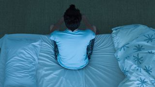 A man sat on the edge of his bed at night struggling with insomnia
