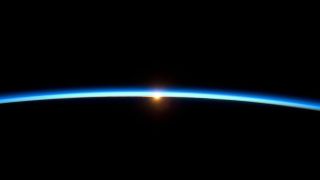 image of Earth's atmosphere appearing as thin blue line above Earth and the sun in the background 