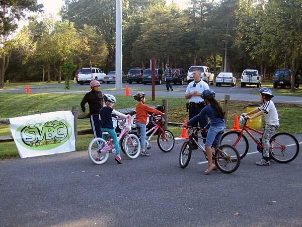 A few kids listen to the local officer who instructs on how to ride safely on the roads to the local trailheads.