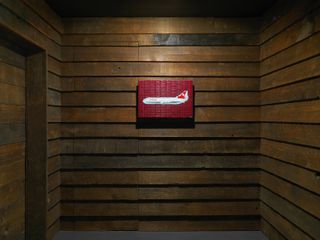 View of a piece of wall art featuring an aeroplane against a dark red background in a room with dark wood panelled walls