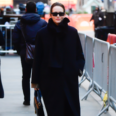 Claire Foy walks down the street wearing a black coat with brown heels boots and a black leather bag.