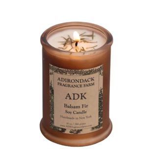 A brown candle with a brown label that says 'Adirondack Fragrance Farm ADK balsam fir soy candle'