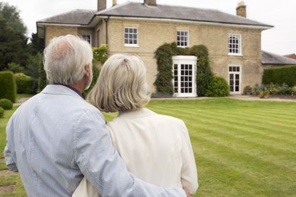 A mature couple looks at their house in the distance.