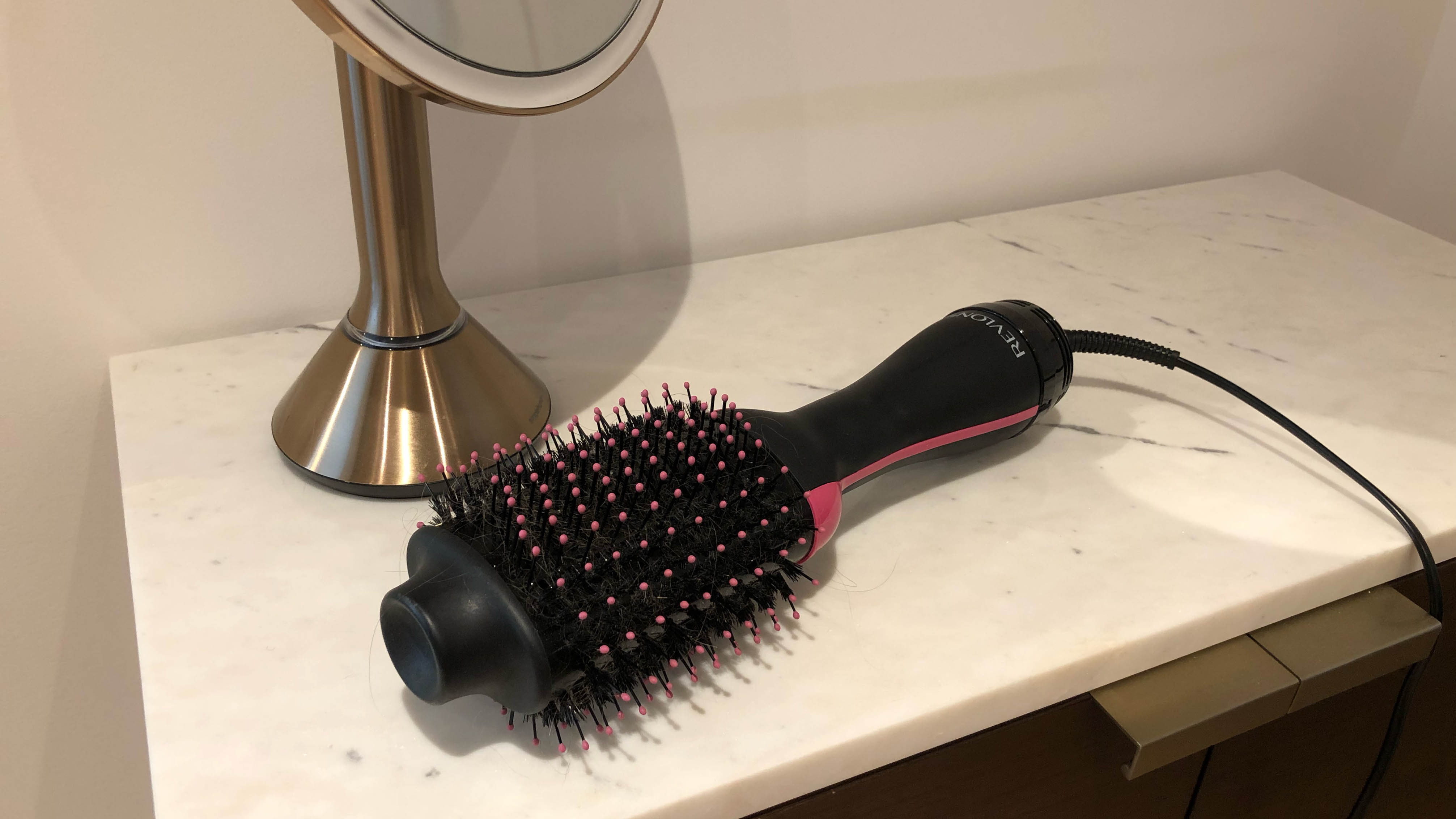 The Revlon One Step Hair Dryer on a cabinet next to a mirror