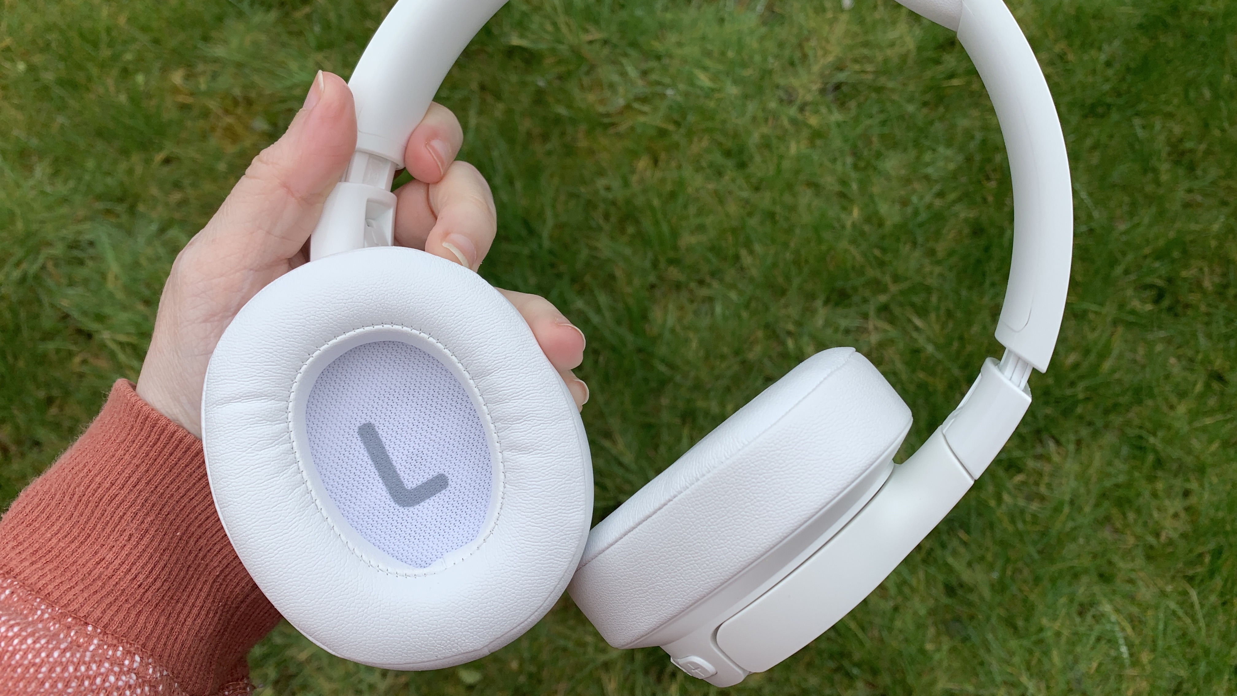 Tampilan dekat bagian dalam cangkir headphone over-ear jbl tune 750btnc berwarna putih dengan latar belakang rumput