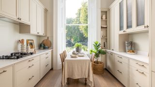 galley kitchen with cream units, wooden floor, window at end of room and dining table in middle of room