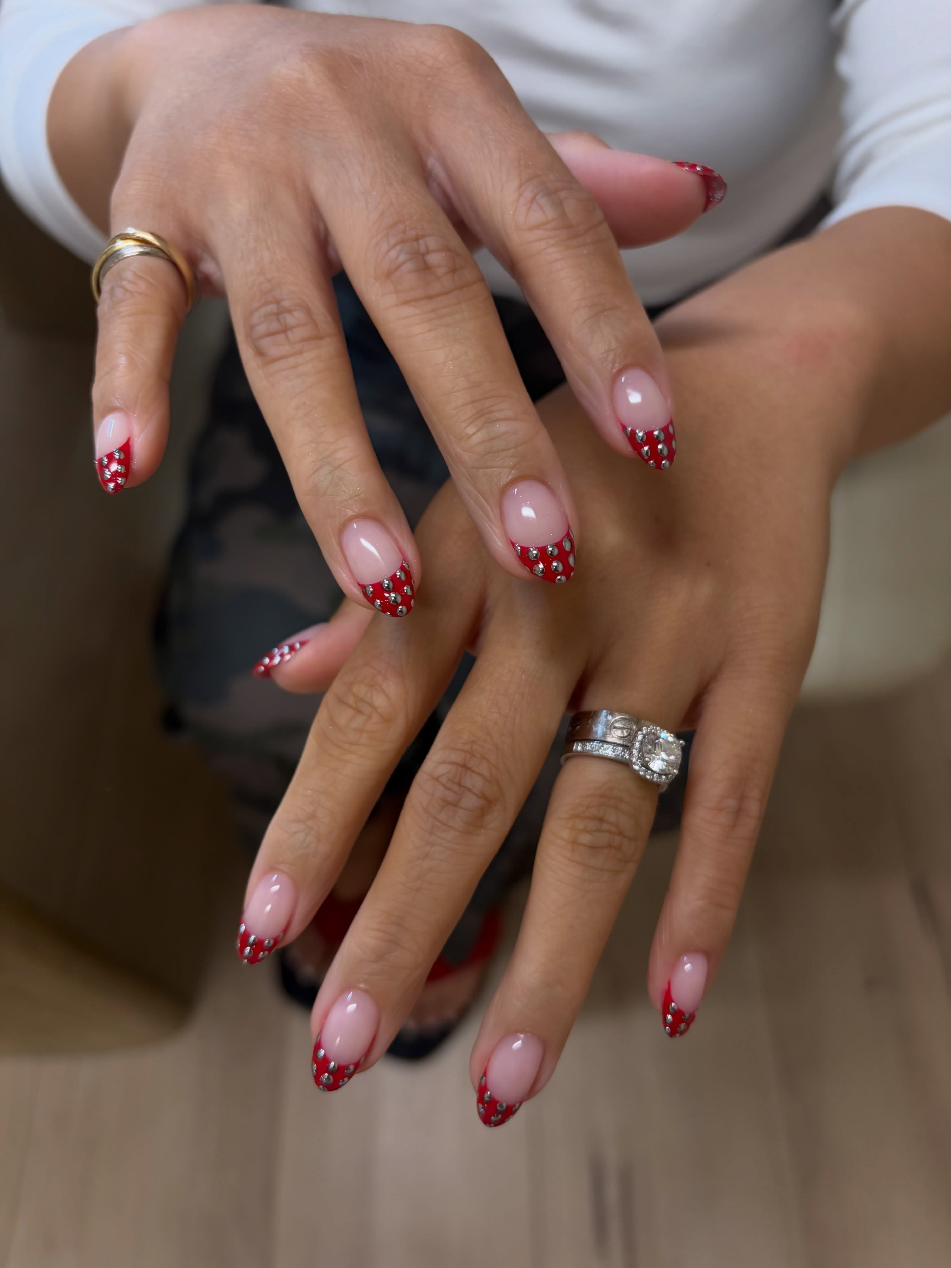 Almond-shaped nails with glossy nude bases, deep red French tips, and small silver polka dots
