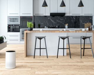 A white air purifier in a modern wooden and white kitchen, with black bar stools, black pendant lights, and black backsplash