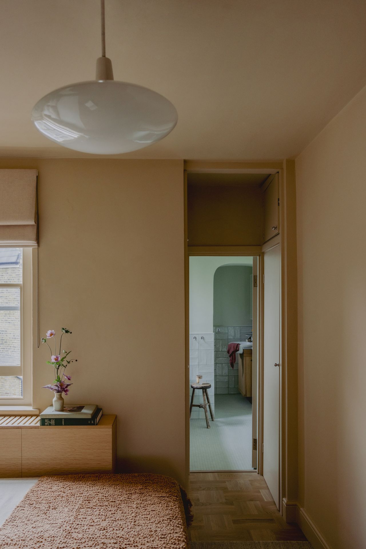 Image of a bedroom painted in a dirty peach/beige color the door to the bathroom is open revealing a light teal/cyan color-drenched bathroom.