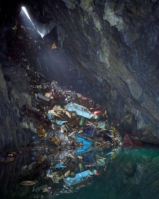 Junk in a cave consists mostly of metal scraps. It reflects on the water below.