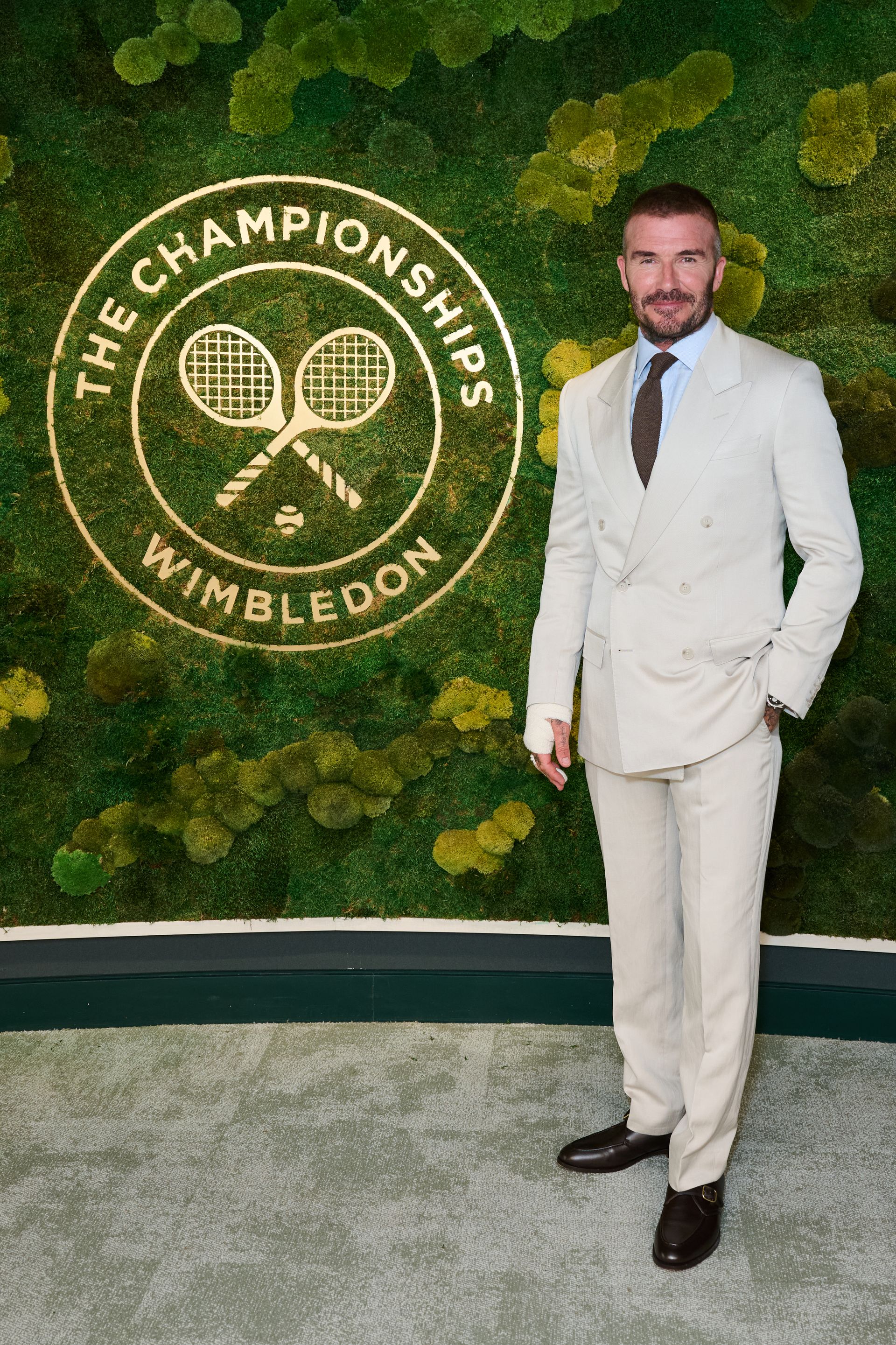 David Beckham arrives at Wimbledon 20205 in a light cream suit with a blue shirt and chocolate brown tie.