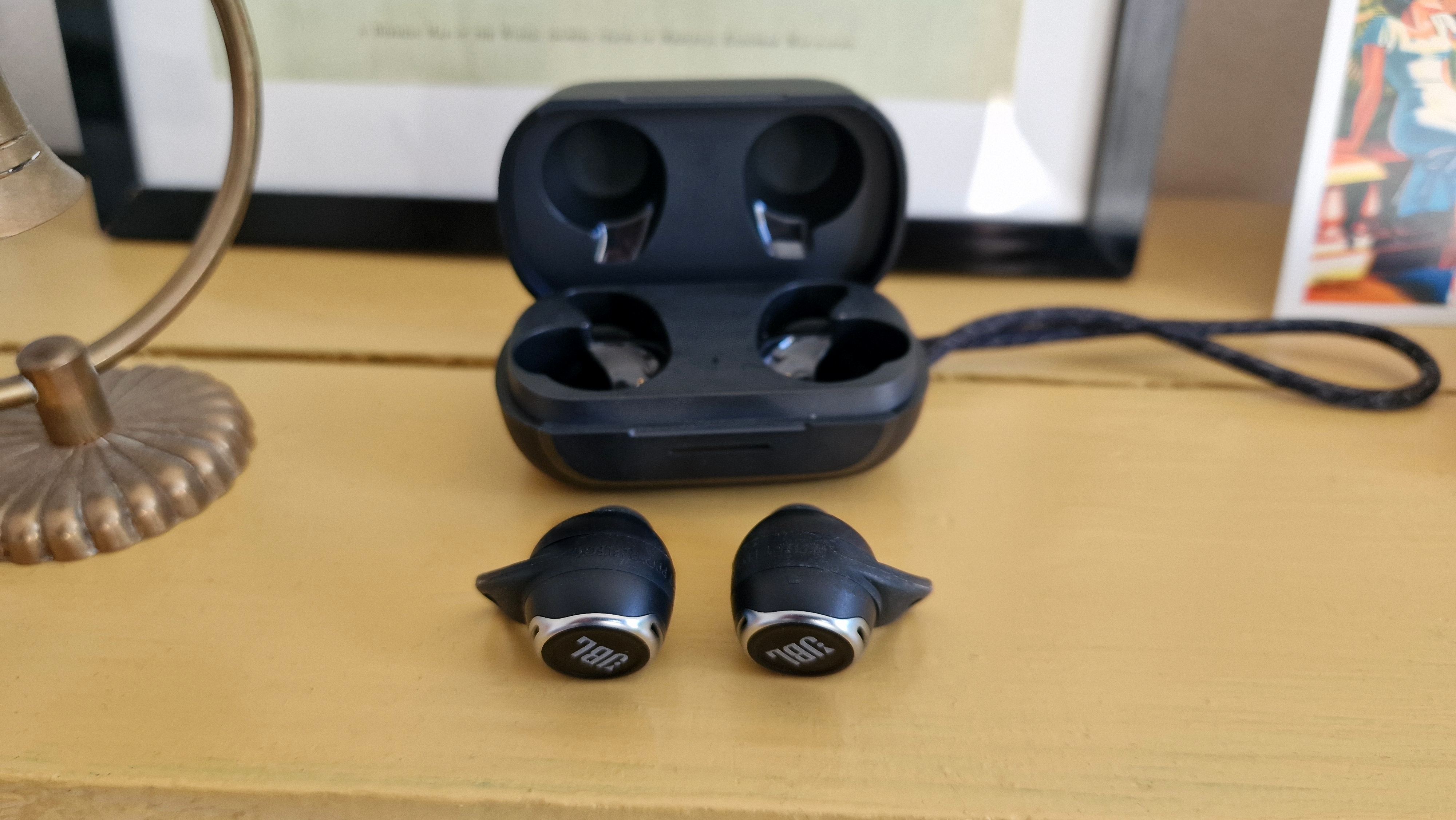 JBL Reflect Flow Pro ligger foran det åbne etui på en gul hylde