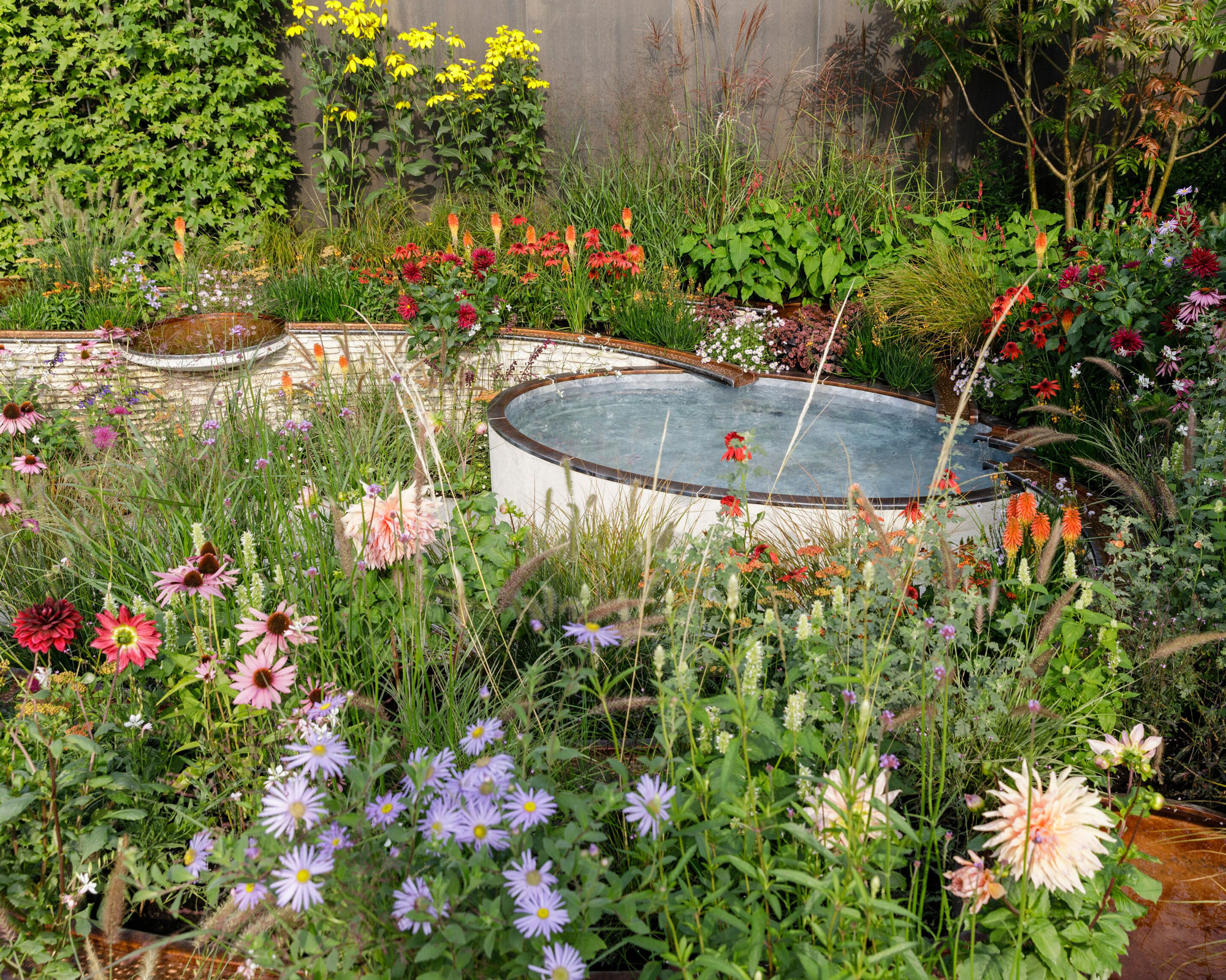small circular freestanding pond landscaped in immersive naturalistic planting