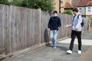 Two teenage boys walking along the pavement with masks on, after learning what being asymptomatic with Covid-19 means