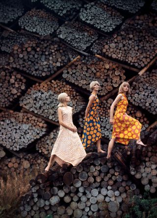 Vogue, November 15, 1965 - Model on the bulwark of a rowboat filled with yellow flowers on a riverbank near Helsinki, Finland, wearing a sleeveless short cotton smock dress printed in yellow and blue waves and black-lacquered wood clogs laced to the knees with blue and yellow straps; by Marimekko