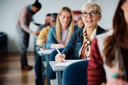 Mature woman writing in notebook during adult education training class in the classroom.