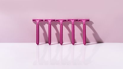 Five pink razors lined up against a pink background