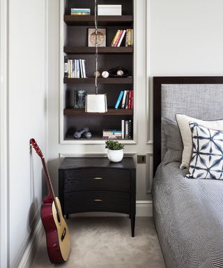 A teenage boys bedroom idea with guitar on the floor, grey bedding and dark wood open shelves built into white walls