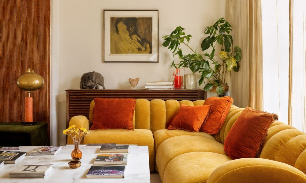 Mustard velvet sofa with orange cushions, marble coffee table, framed art, plants and vintage sideboard.