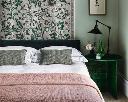 Green bedroom with pink throw and patterned wallpaper