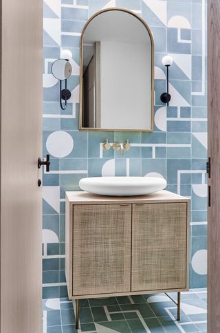 blue patterned tiled on the walls and floors of a bathroom with a wood vanity and arch mirror