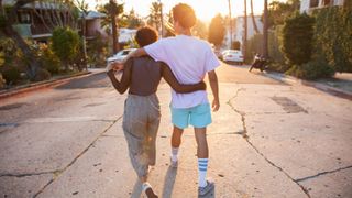 Young couple with their arms around each other walking down street - stock photo
