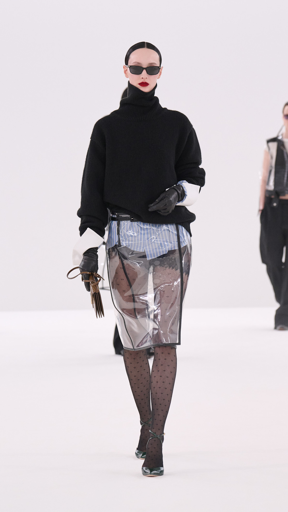 a Tom Ford model wearing a black turtleneck, PVC pencil skirt, and polka dot tights