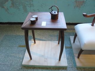Square, smooth table with a small kettle and two cups, on a wooden plinth