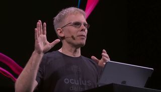 John Carmack speaking in front of a lectern with black and pink background behind