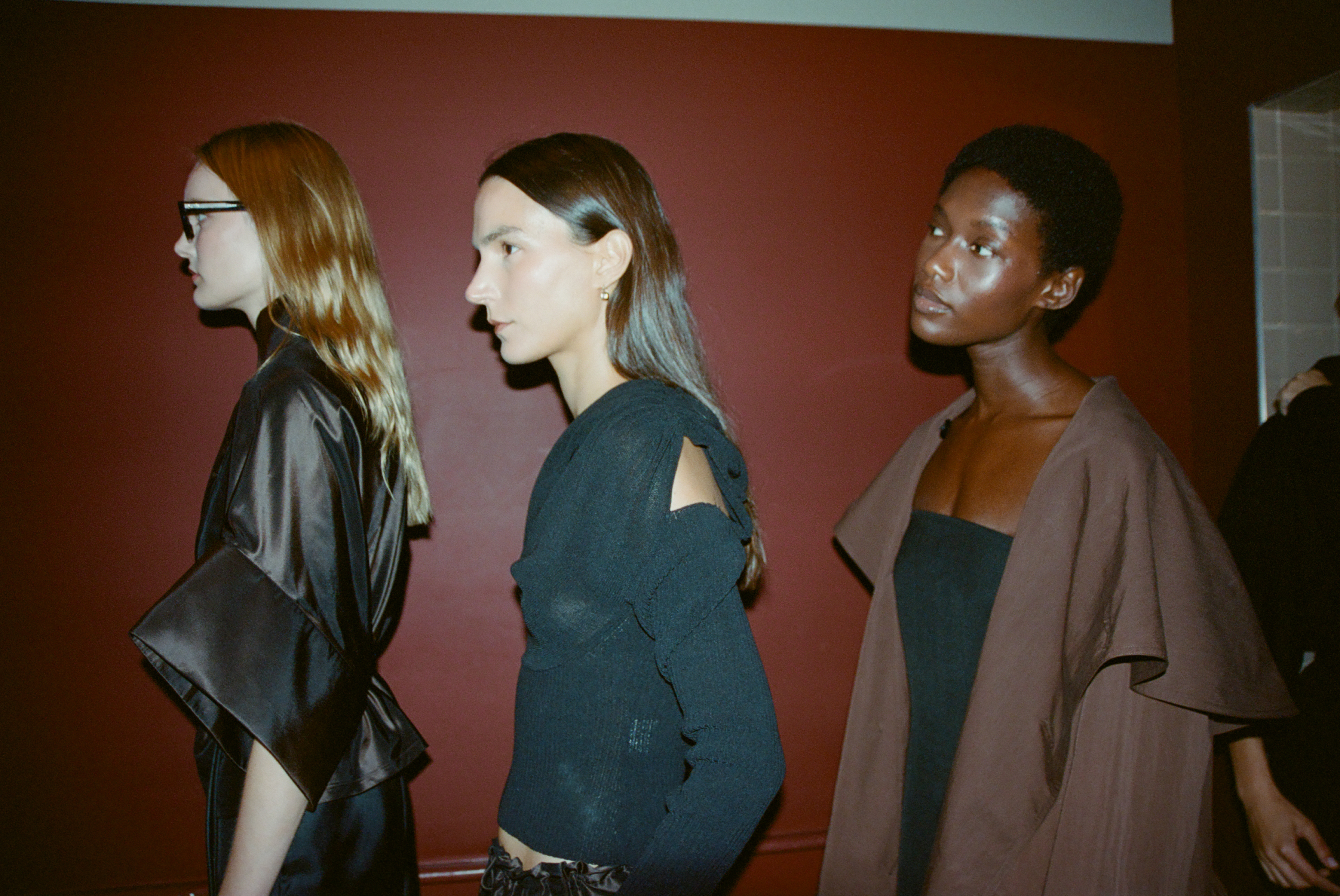 three models standing against a red wall wearing navy blue jackets with glowing skin