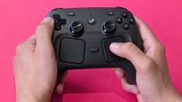 Valve Steam Controller (2026) held in two hands against a magenta card background